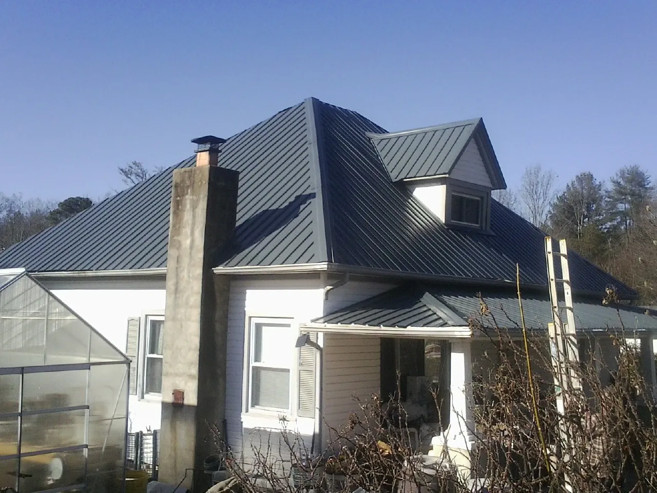 Dark blue standing seam metal roof on a white farmhouse with dormer — Slate & Tile Roof Repair by Roofing Brothers in Underwood