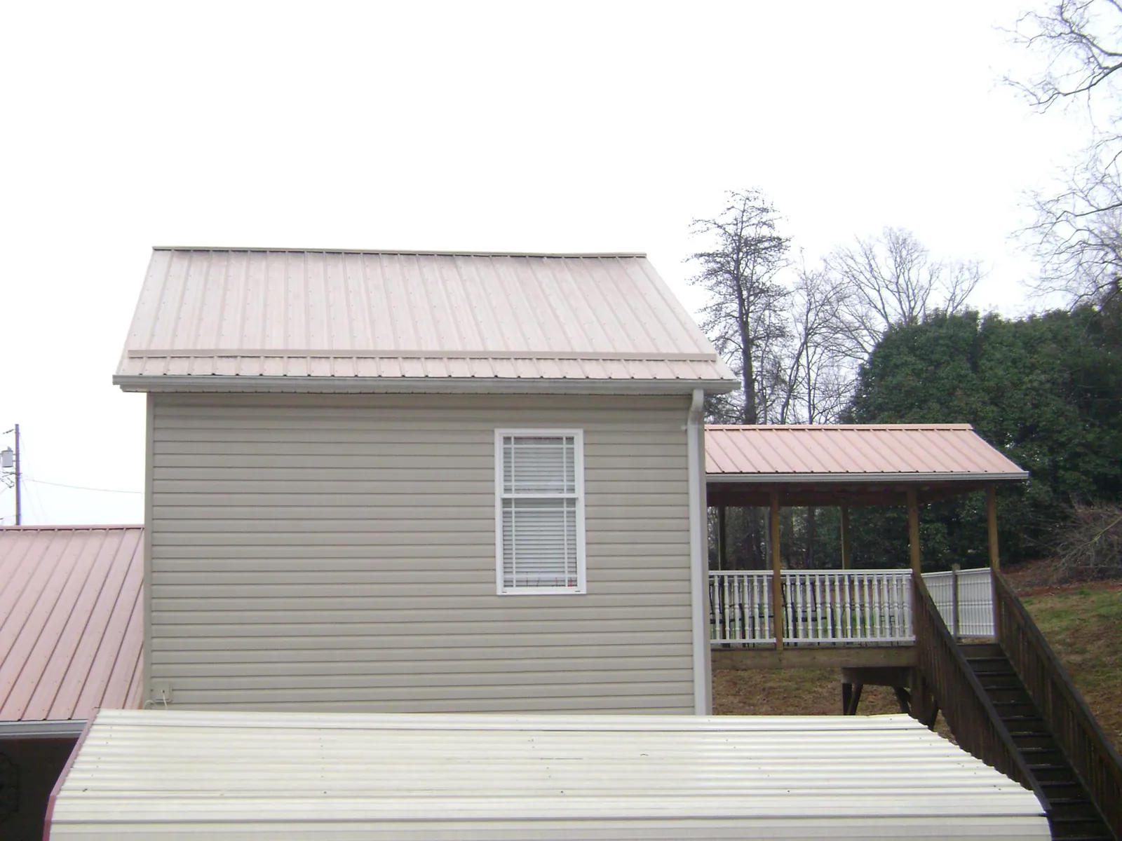 Tan metal roofs on a two story addition and attached porch, from a Roof Replacement job in Underwood